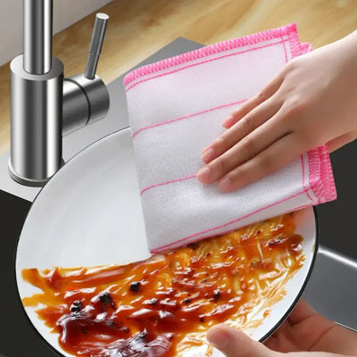 Hand using a cotton dishcloth to clean a plate with sauce at a kitchen sink.